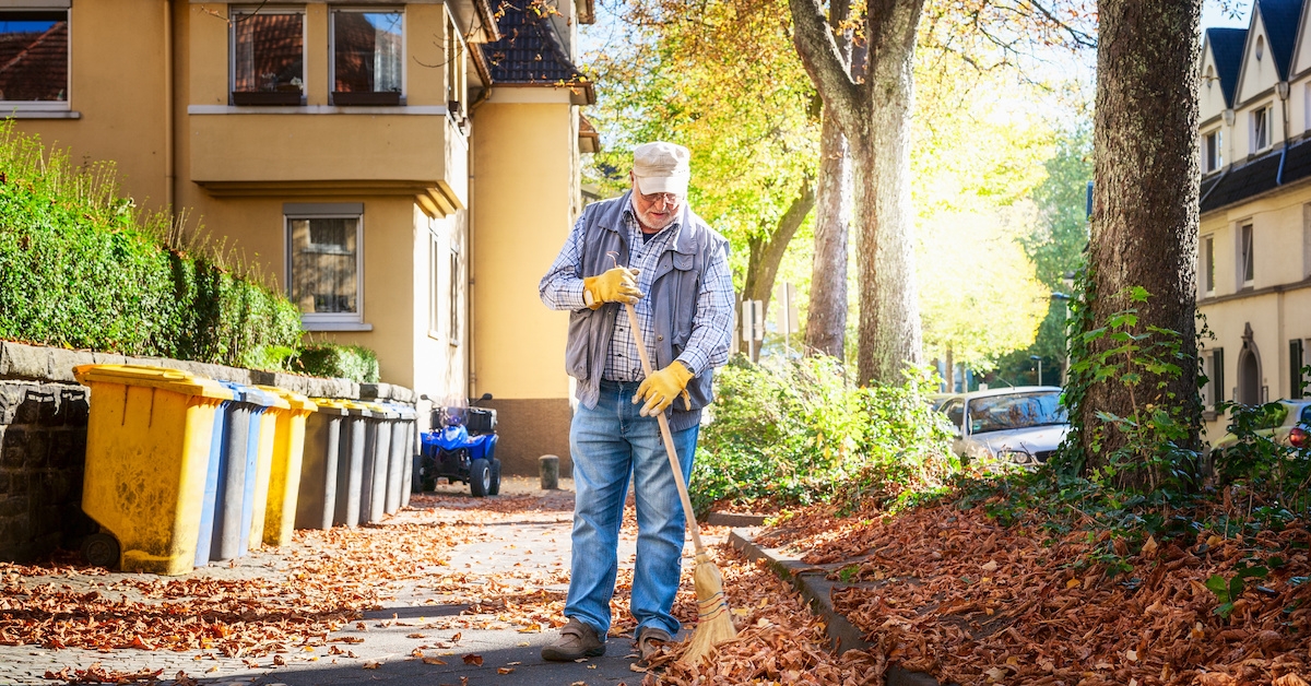 An older man sweeps leaves in his driveway