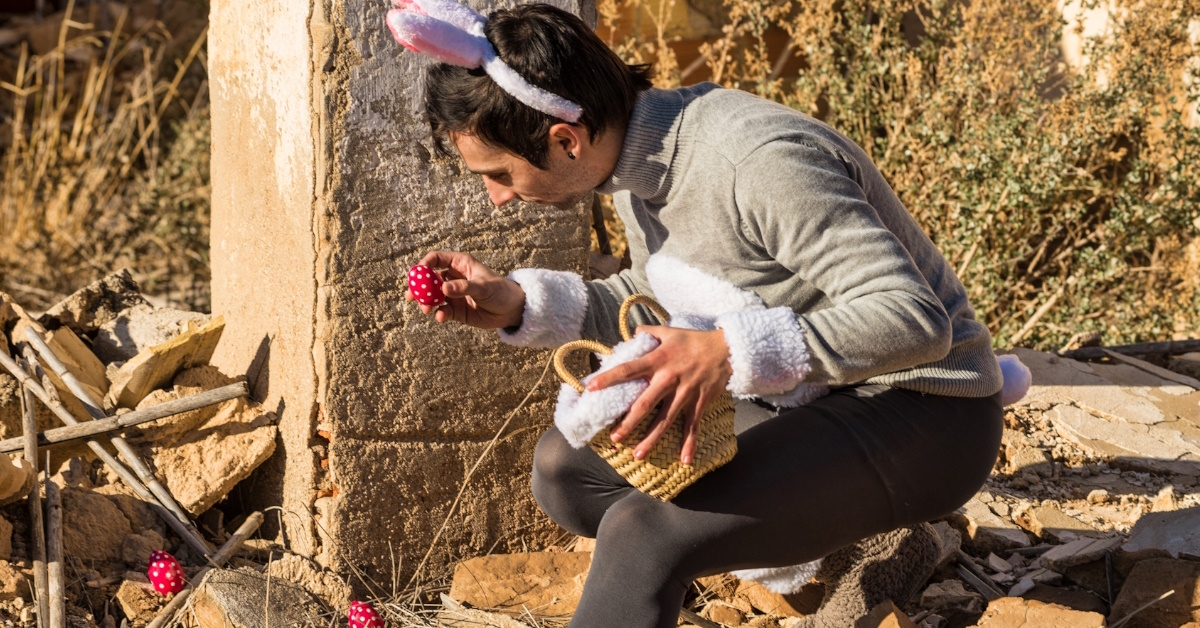 man wearing funny easter suit with headband hiding small red color eggs in woods