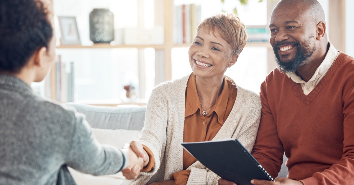female finance advisor shaking hand with mature couple sitting on couch