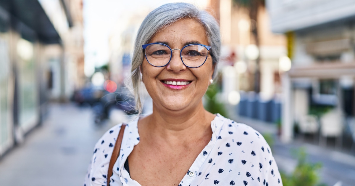 senior woman with grey hair wearing glasses smiling confidently in street