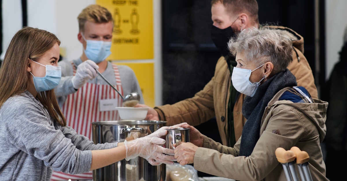young teenage volunteers serving soup to homeless people during pandemic
