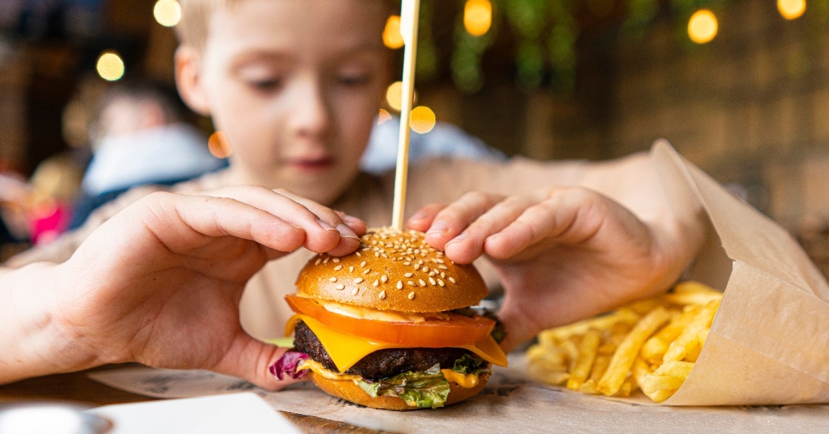 young boy eating a mini burger with fries in a cafe.
