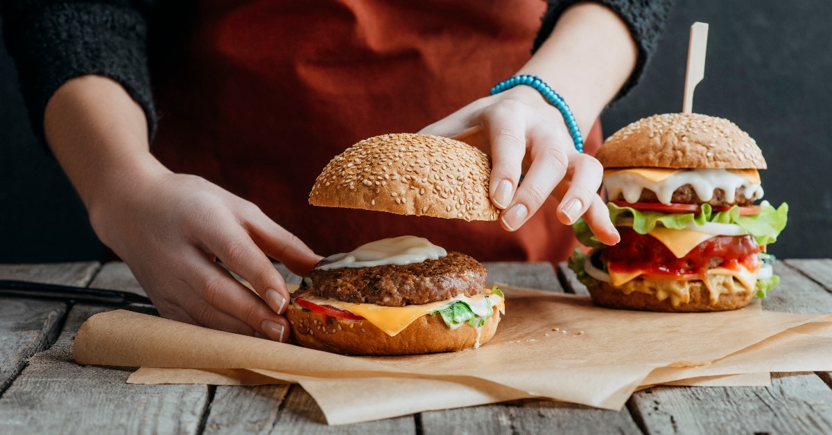 girl in apron making homemade cheeseburgers on baking paper on wooden tabletop