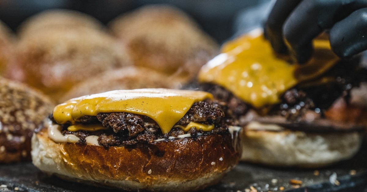 preparing a gold plated burger with cheddar on the grill