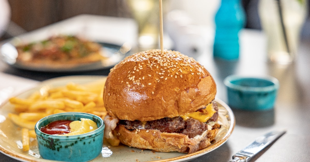 large burger in a plate with fries and sauces in the restuarant.