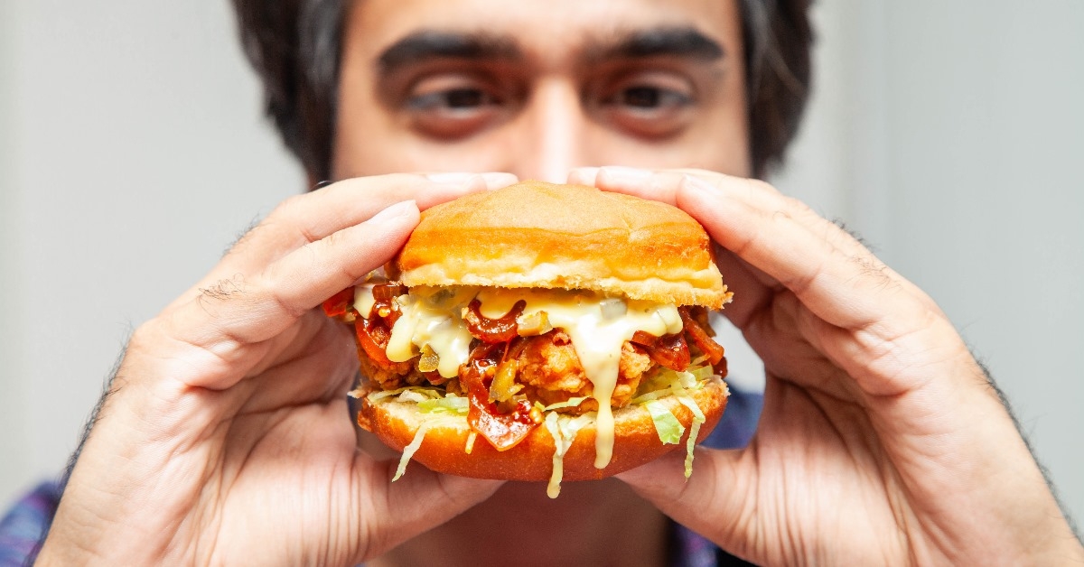 eastern man looking at crispy chicken burger with melted cheese and is about to eat it.