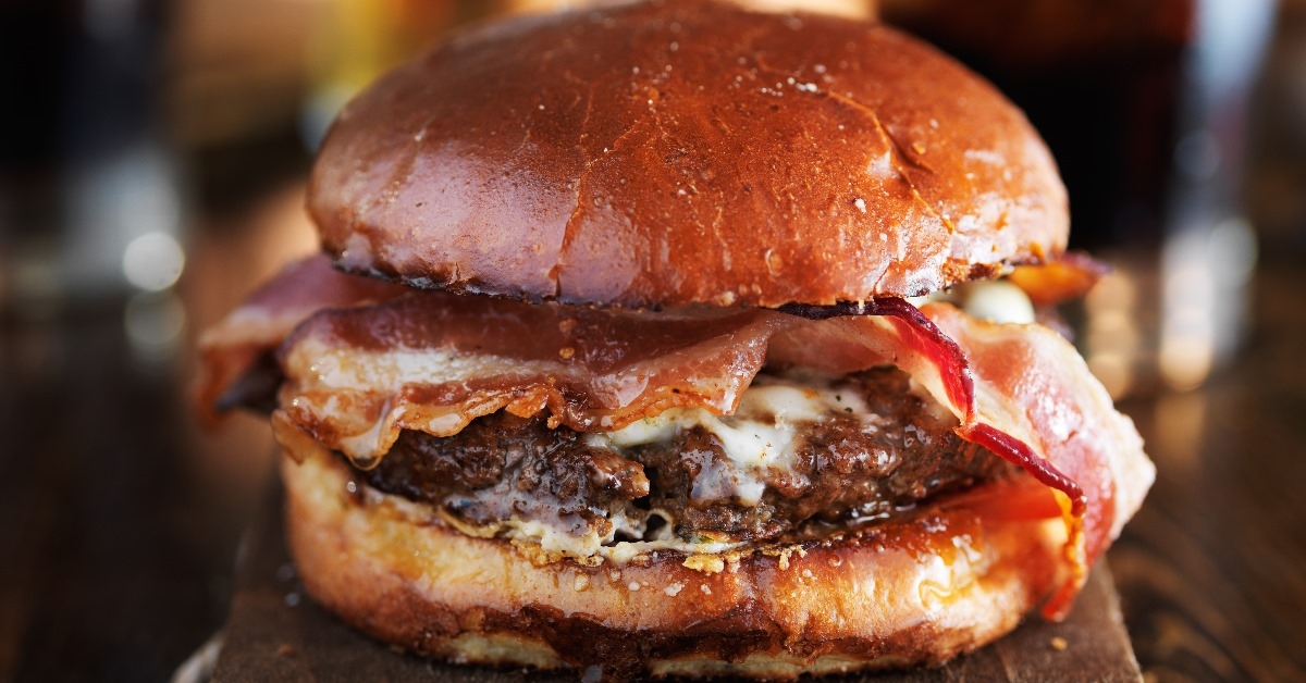 juicy gourmet cheeseburger with melted pepper jack and strips of crispy bacon with ice chilled cola in background