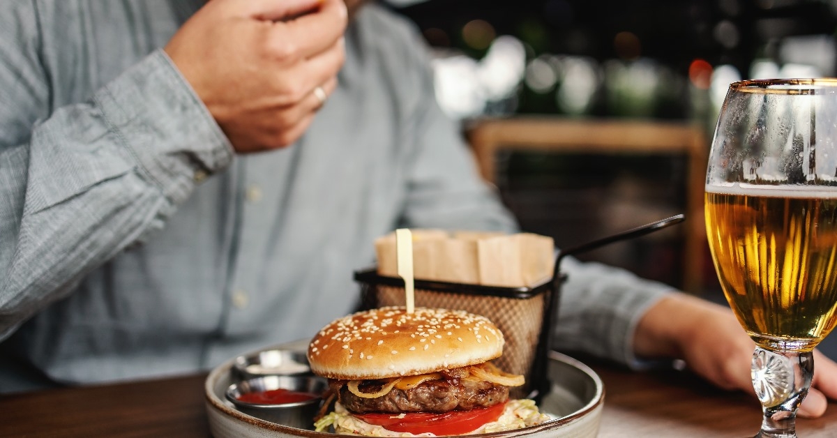 middle aged bearded hungry man sitting in restaurant and eating delicious burger
