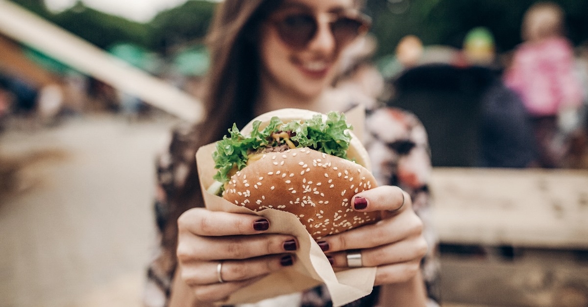 stylish hipster woman smiling and showing her juicy hamburger in a festival.
