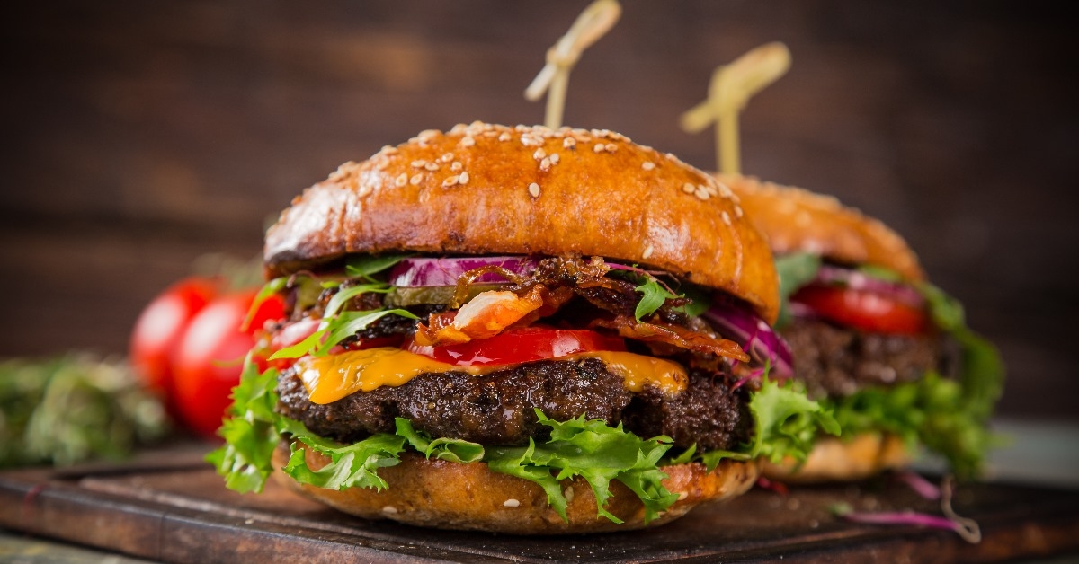 tasty burgers with melted cheese on wooden table with some vegitables