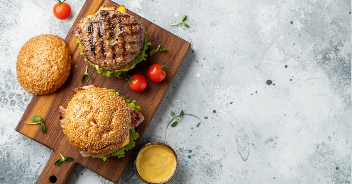 tasty grilled home made burger with beef, tomatoes, cheese, lettuce and sauce on a wooden serving tray 