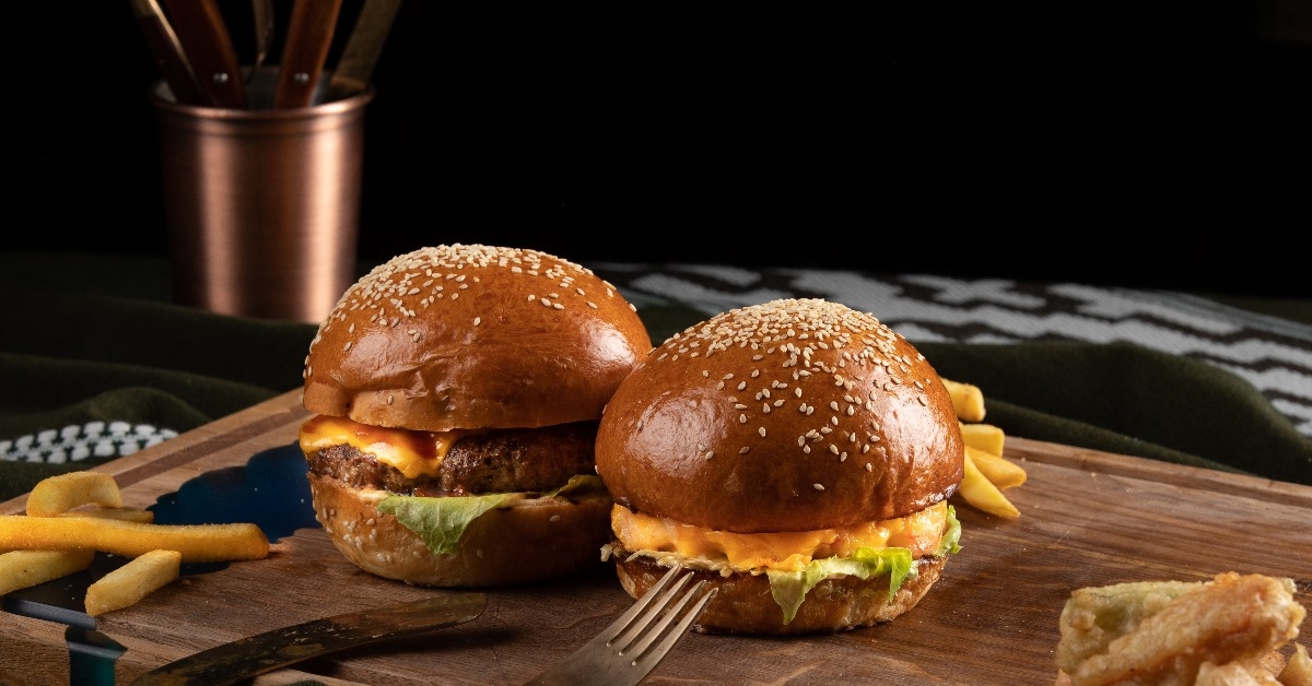 two gourmet tasty steak burgers on a wooden Tray, with fries and a set of fork and knife.