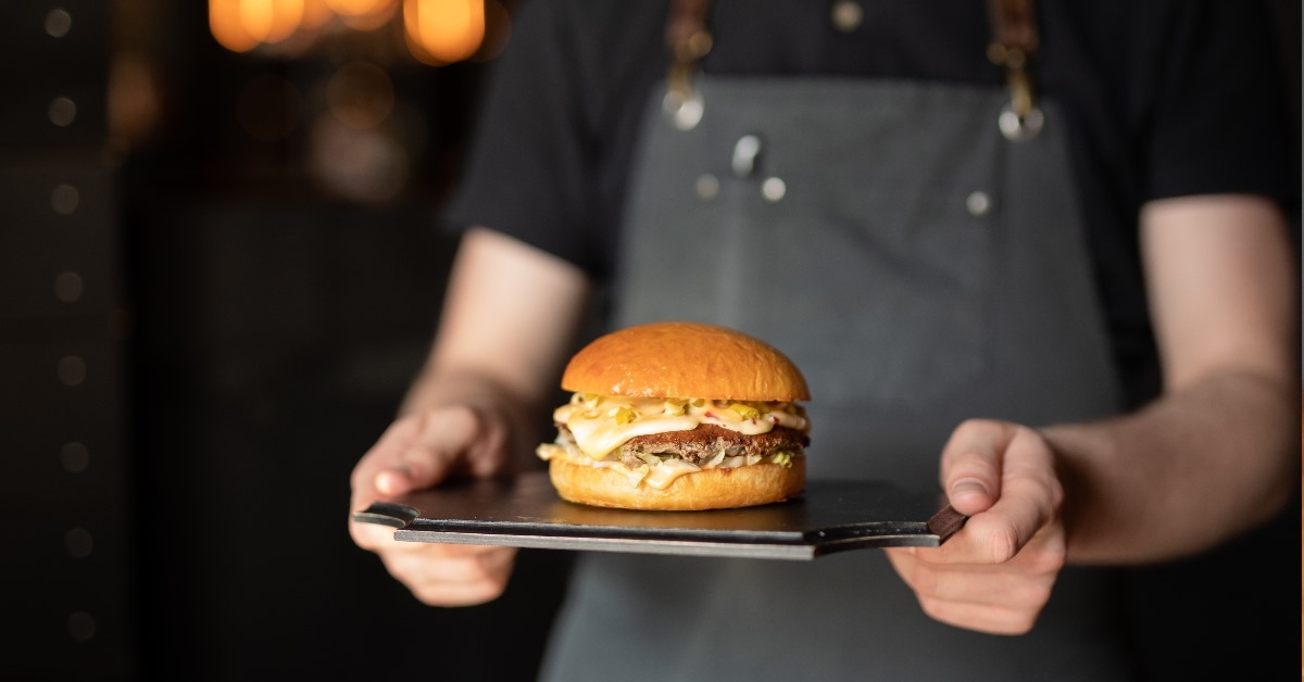 waiter carrying burger for the client in a dark brown tray.