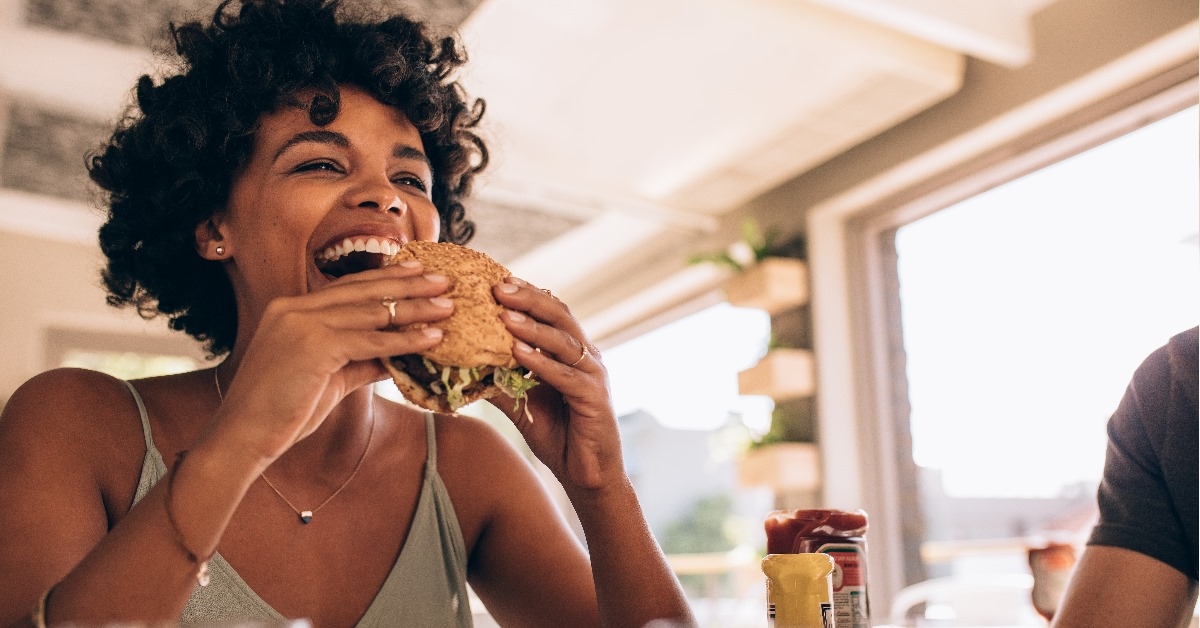 young woman with short curly hairs enjoying burger at restaurant