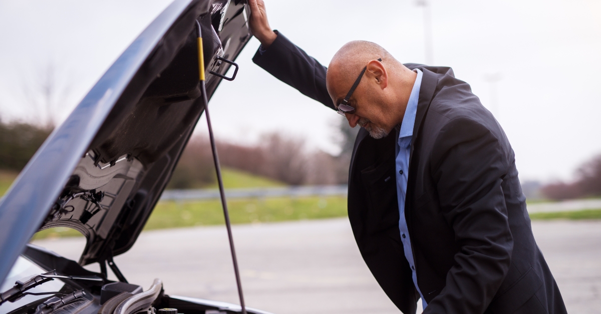businessman in the suit is looking under the car hood