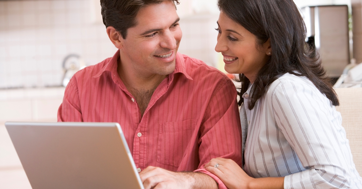 couple in kitchen using laptop and smiling