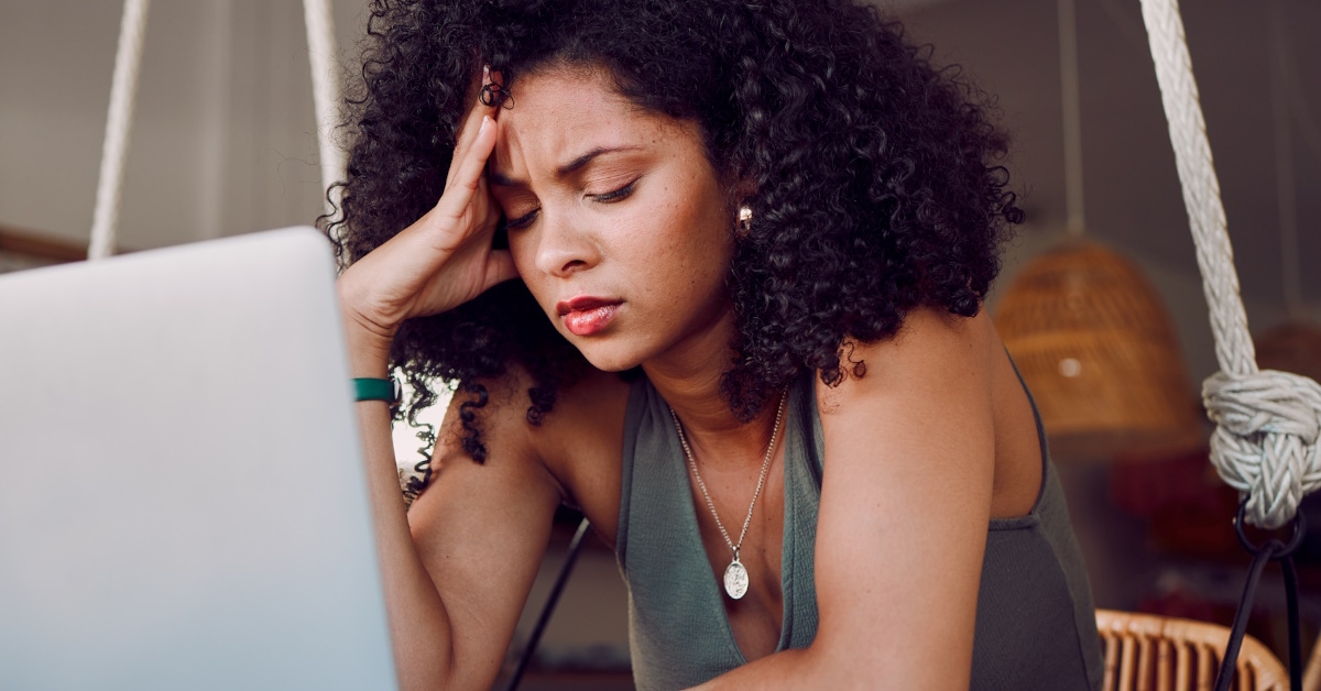 african american female student sitting in front of laptop holding head in stress due to work burden