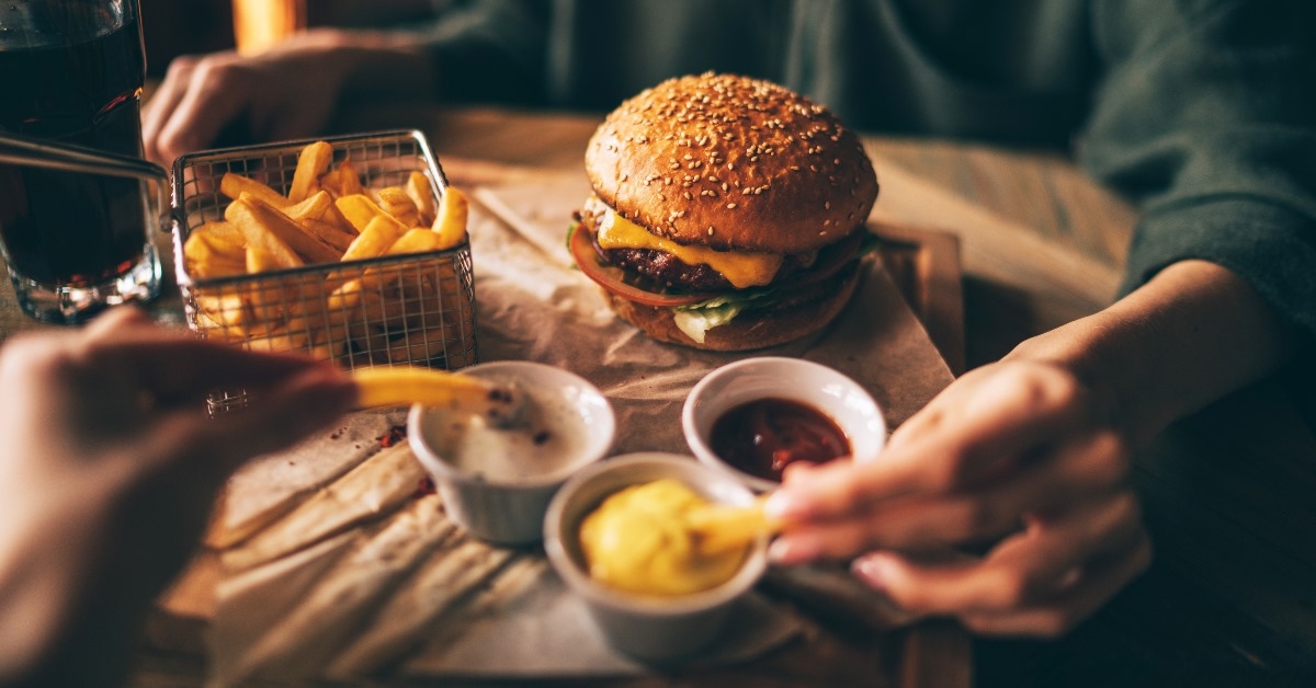 Friends enoyingTasty grilled beef burger with fries, sauces and mayonnaise served on of brown serving tray