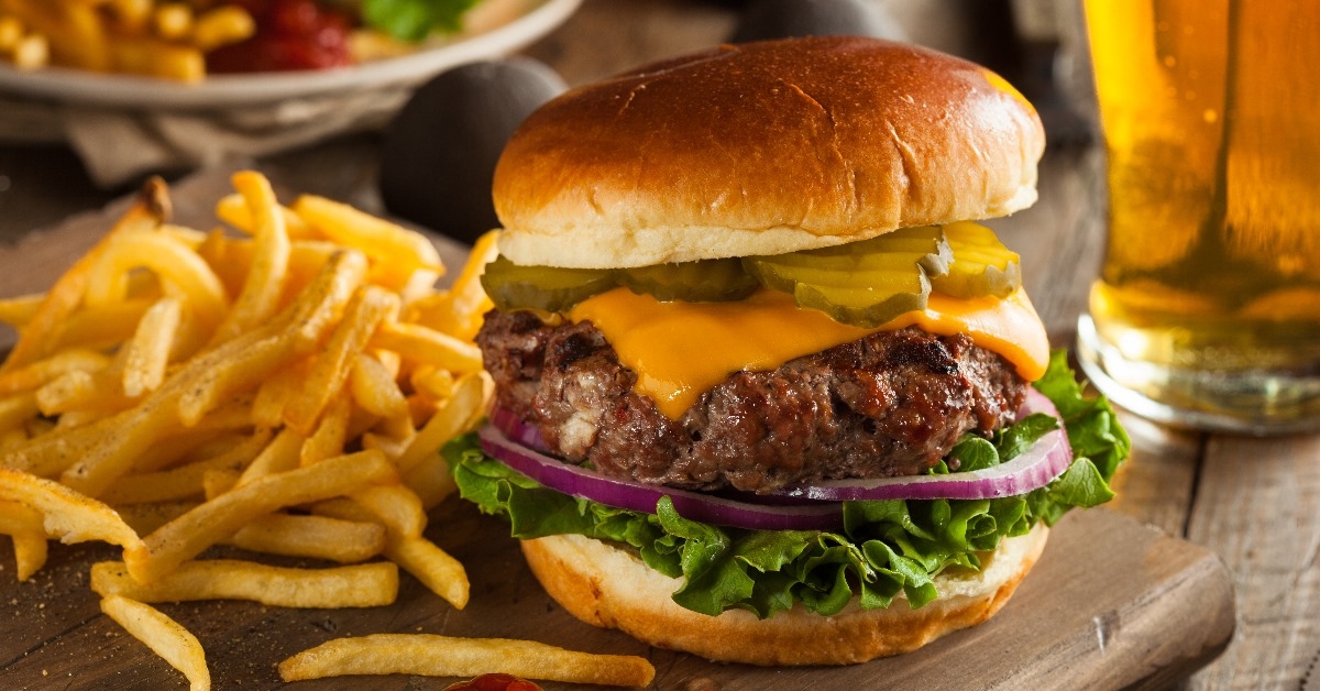 grass fed bison hamburger with melted cheese and sliced vegitables on a wooden serving tray
