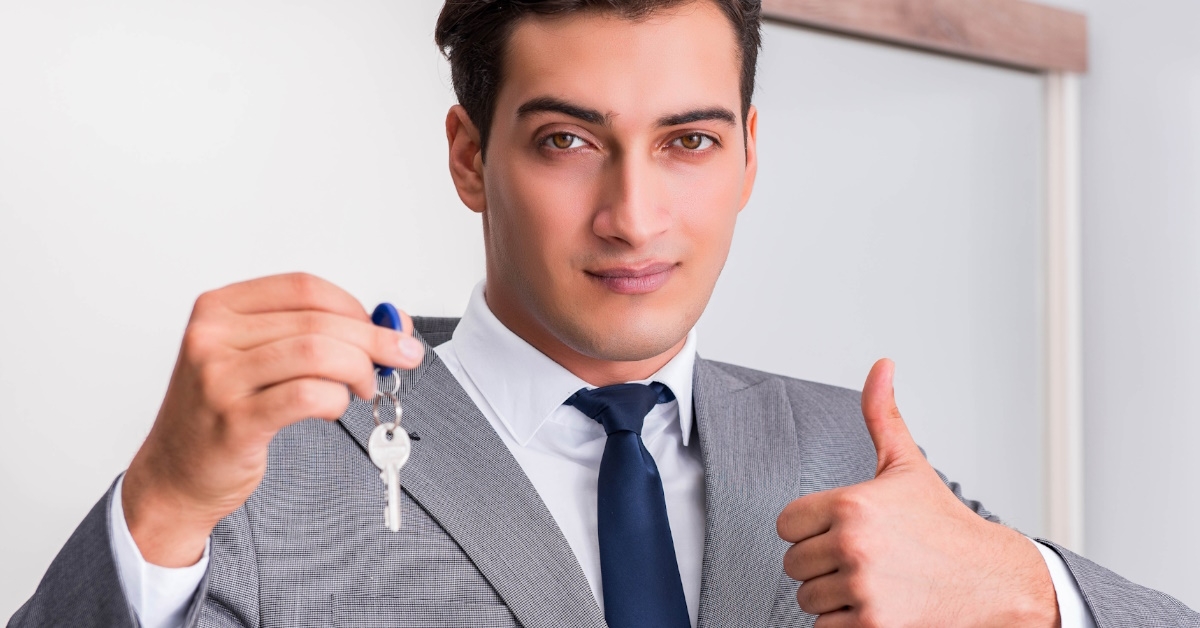 male real estate agent in grey suit doing thumbs up sign while holding new house keys