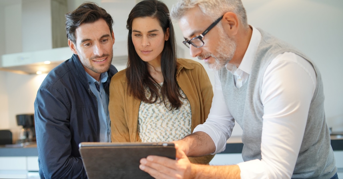 salesman using tablet to show kitchen design to young couple