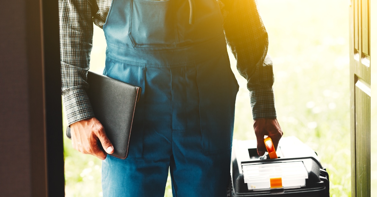 service man entering house while holding tool box and document file