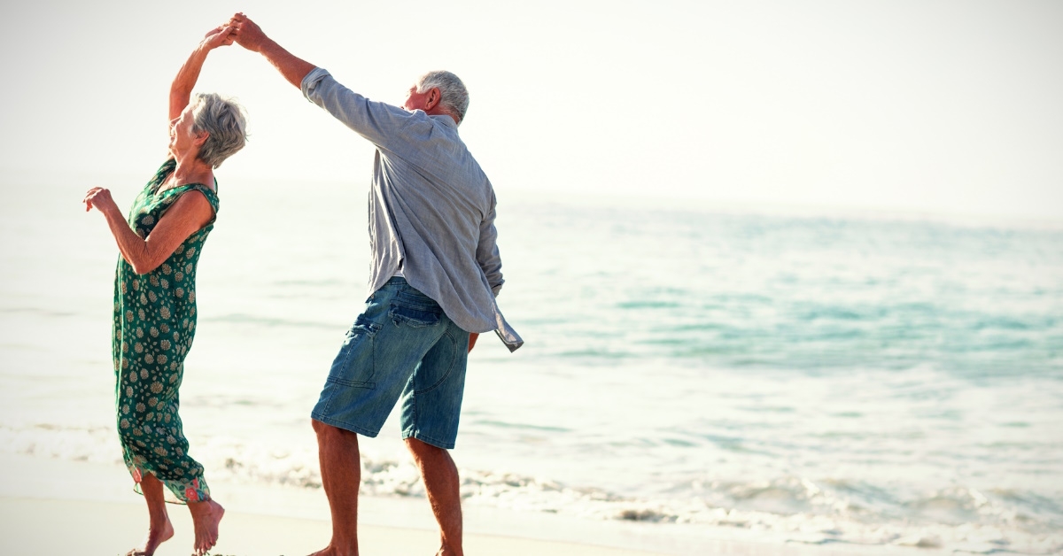 happy senior couple dancing at beach 