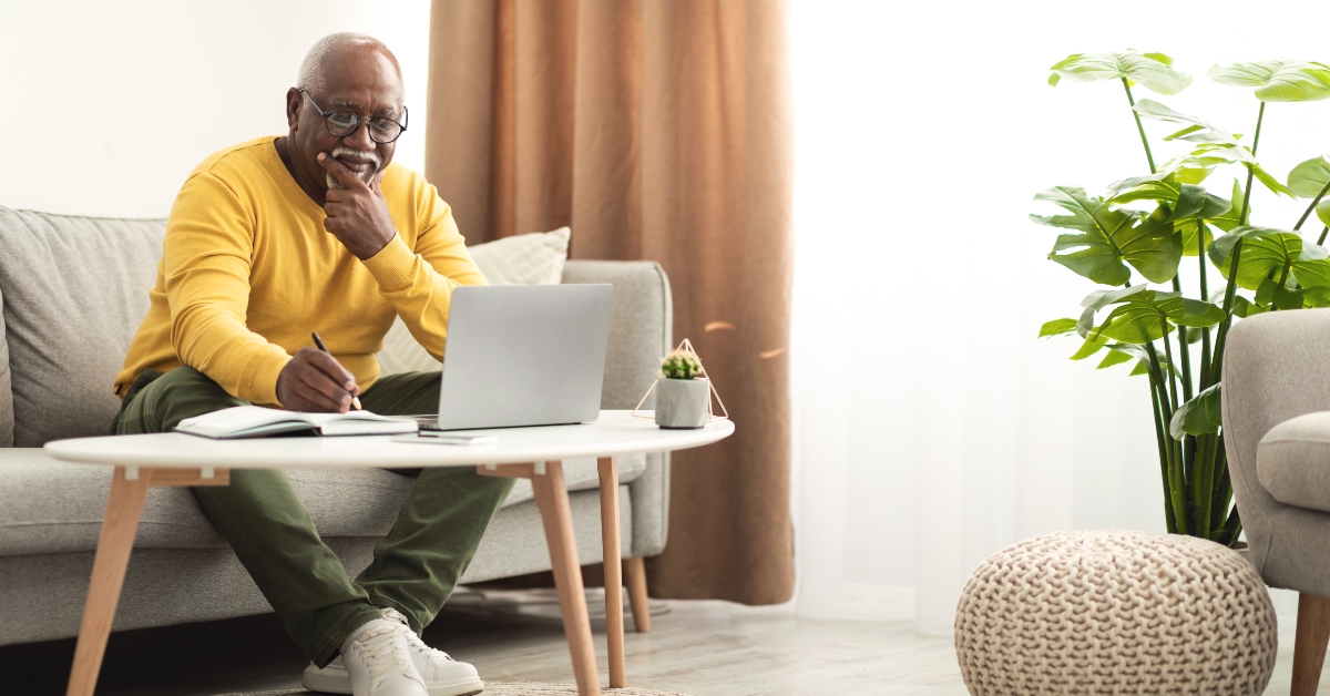senior black male using laptop working online taking notes