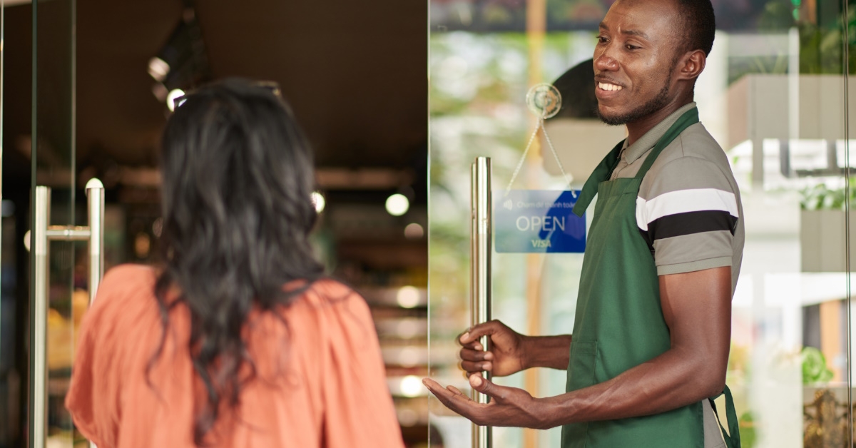 african american supermarket employee welcoming a female customer at the entrance