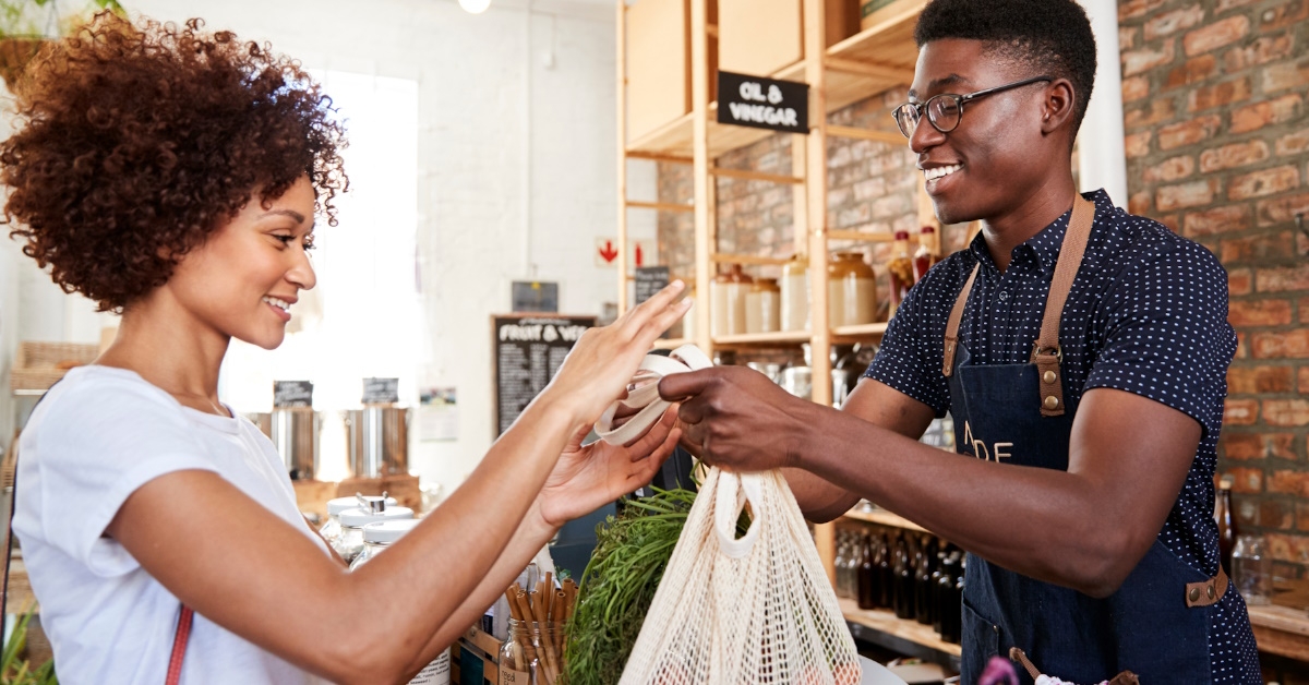 african american woman paying money to cashier after shopping at sustainable grocery store