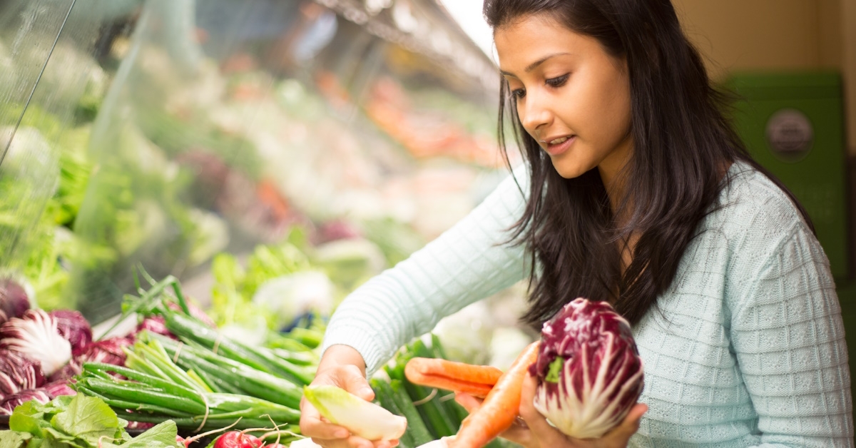woman in grocery store picking up vegetable to buy 