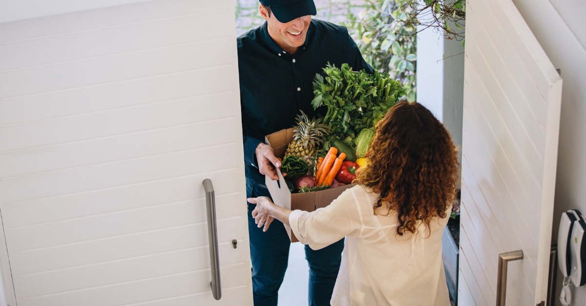 delivery boy giving box full of grocery to woman at home