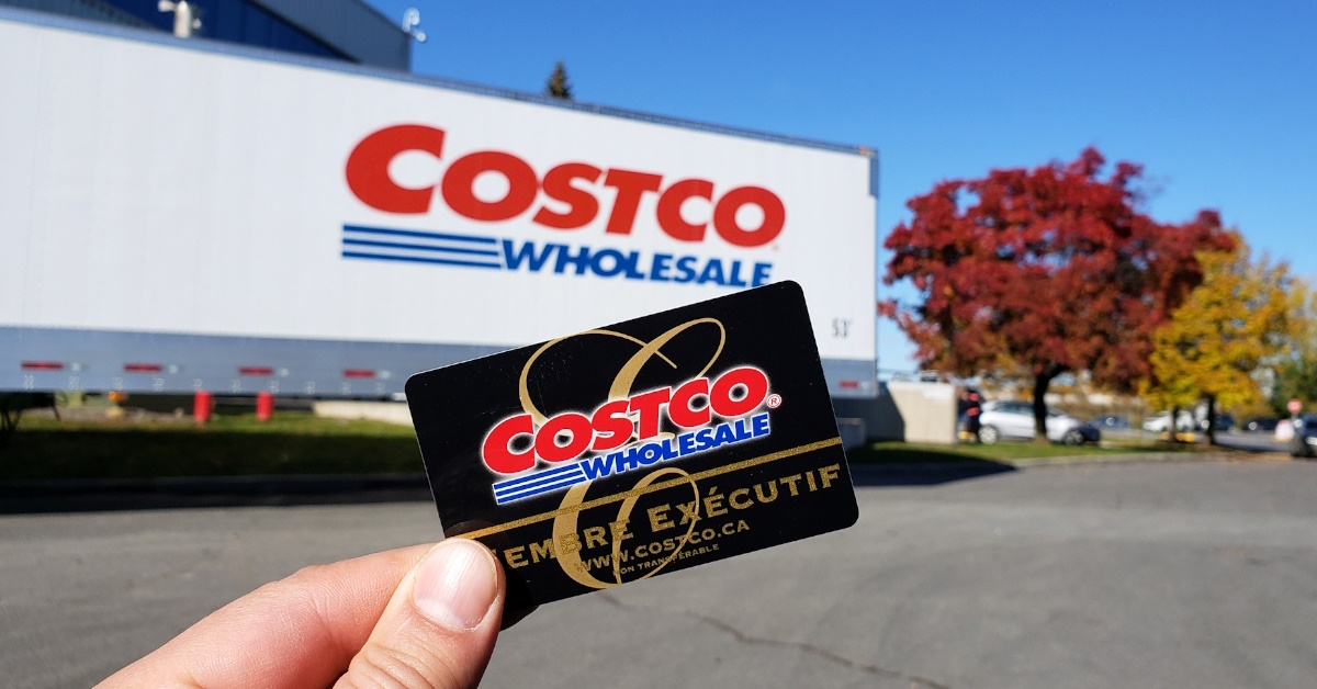 male hand holding a costco membership card with a costco delivery truck in the background
