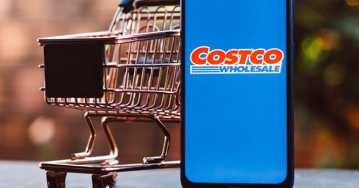 logo of Costco Wholesale Corporation displayed on a smartphone along with a shopping cart in the background