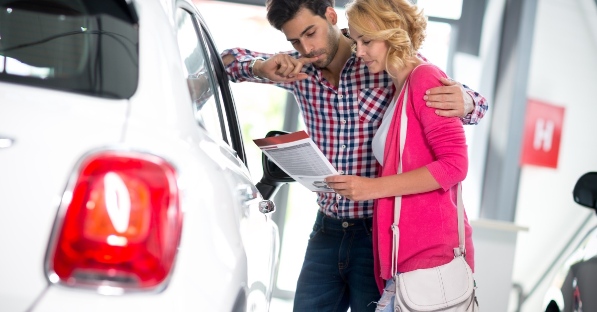couple standing besides car in showroom reading policies before purchasing vehicle