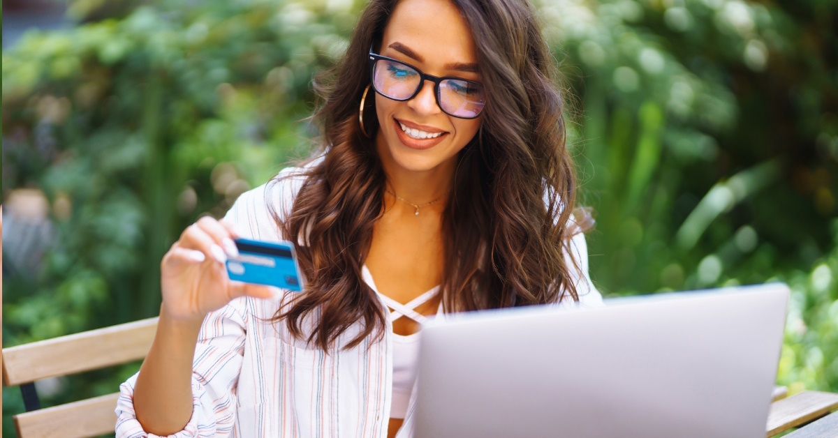 woman sitting at outdoor cafe using card to make online transaction on laptop