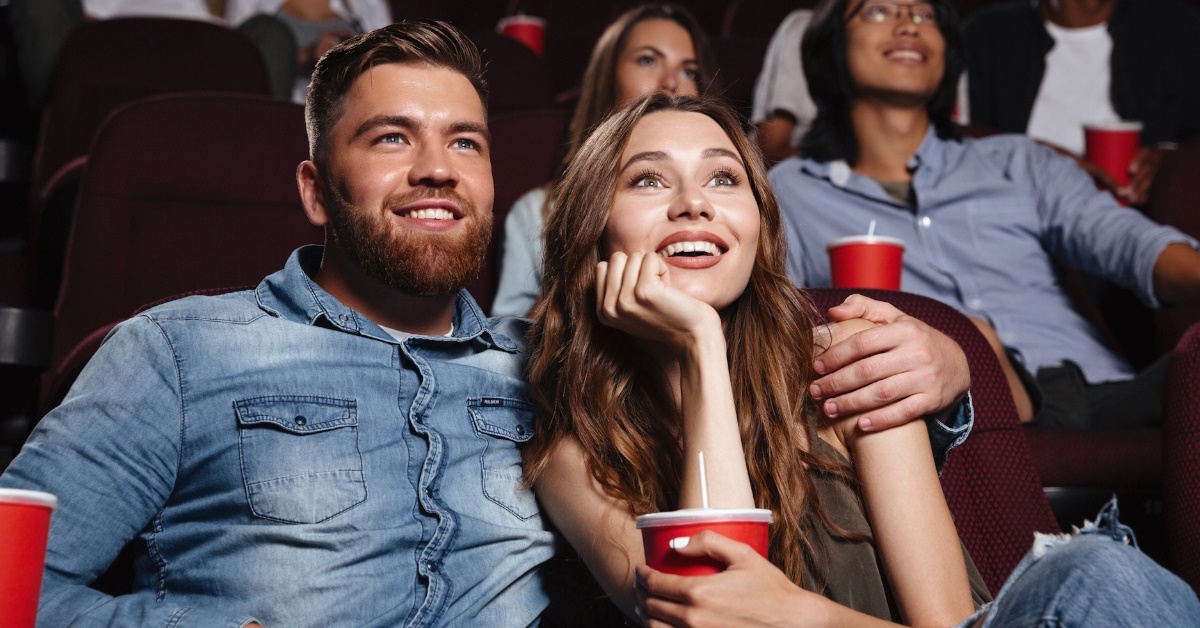 young couple sitting in rows while holding cold drinks watching movie in cinema