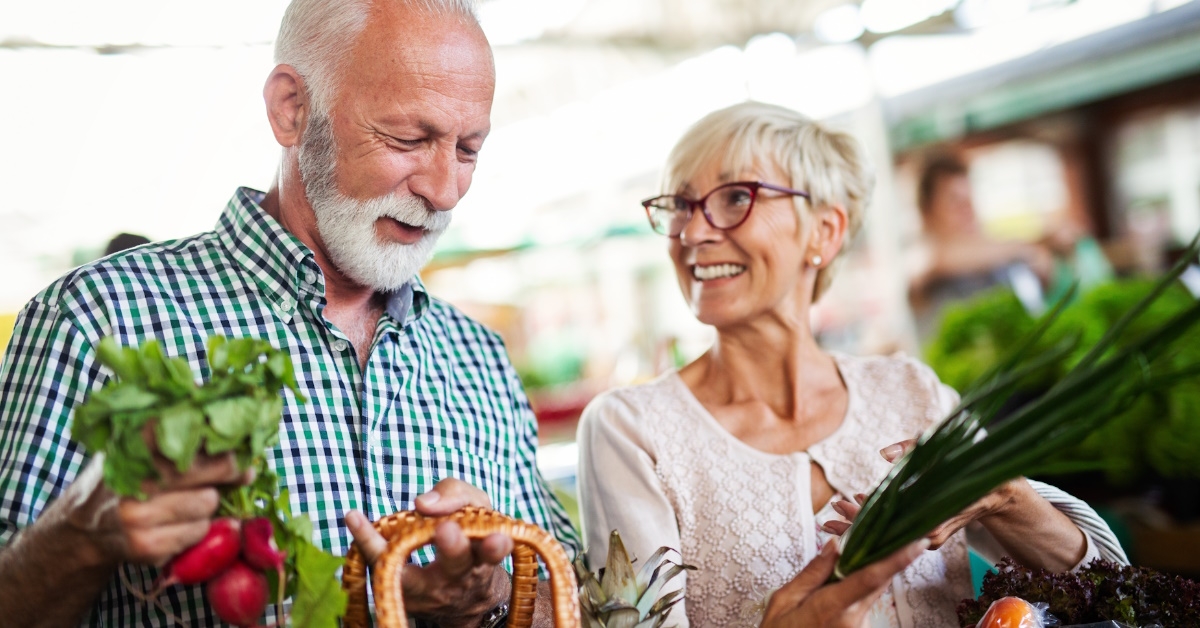 Happy senior couple holding baskets of fresh fruits and vegitables after purchasing from shop.