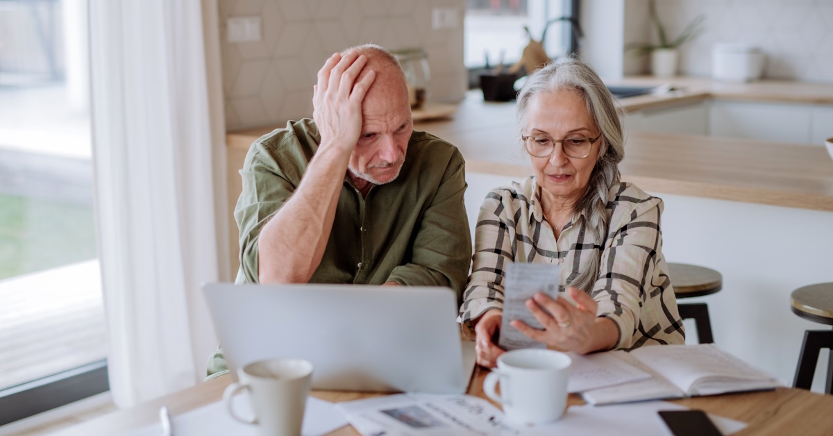 Stressed senior couple calculate expenses or planning budget together while sitting on the table with documents and laptop at home.