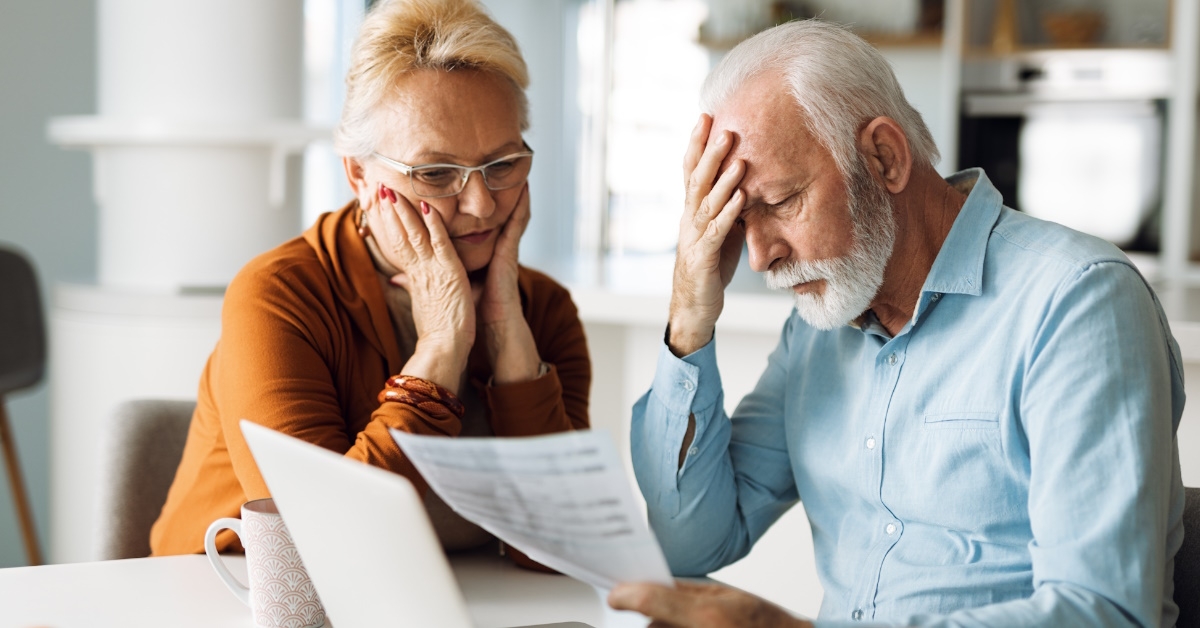 Worried senior couple feeling stressed while paying their bills over Internet while sitting on the table at home.