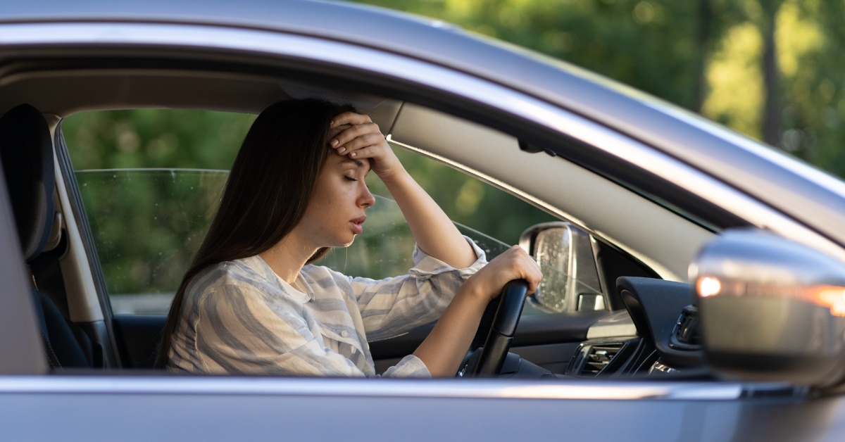 Stressed girl with headache touching forehead with hand is displeased with heat inside vehicle