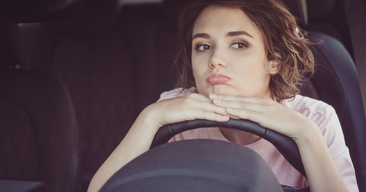unhappy cute young lady driver sit putting her face and hands on steering wheel,looking at traffic jam.