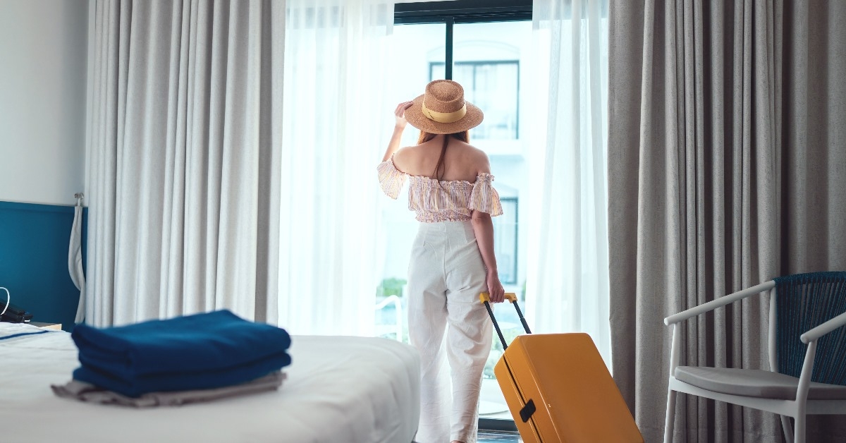 beautiful woman wearing sun hat checking into hotel room with luggage