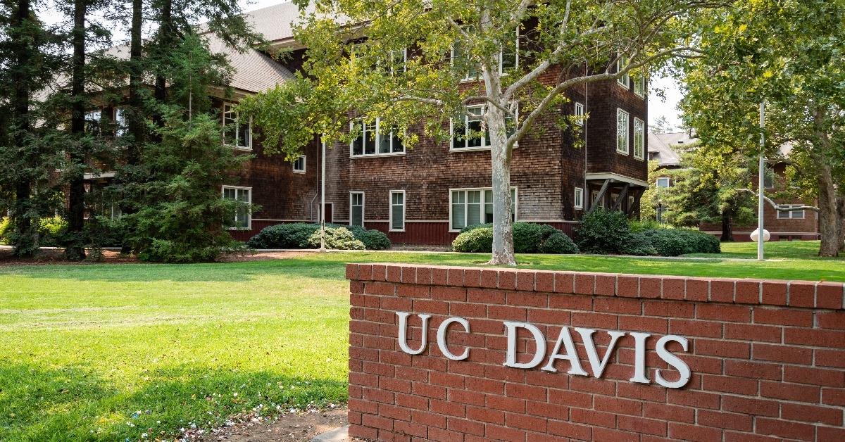 brick gate entrance to uc davis with dutton hall in background surrounded with lush green trees