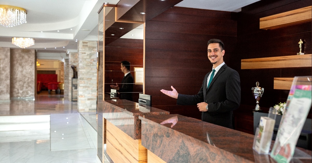 male receptionist wearing suit standing in reception welcoming guest with smile 