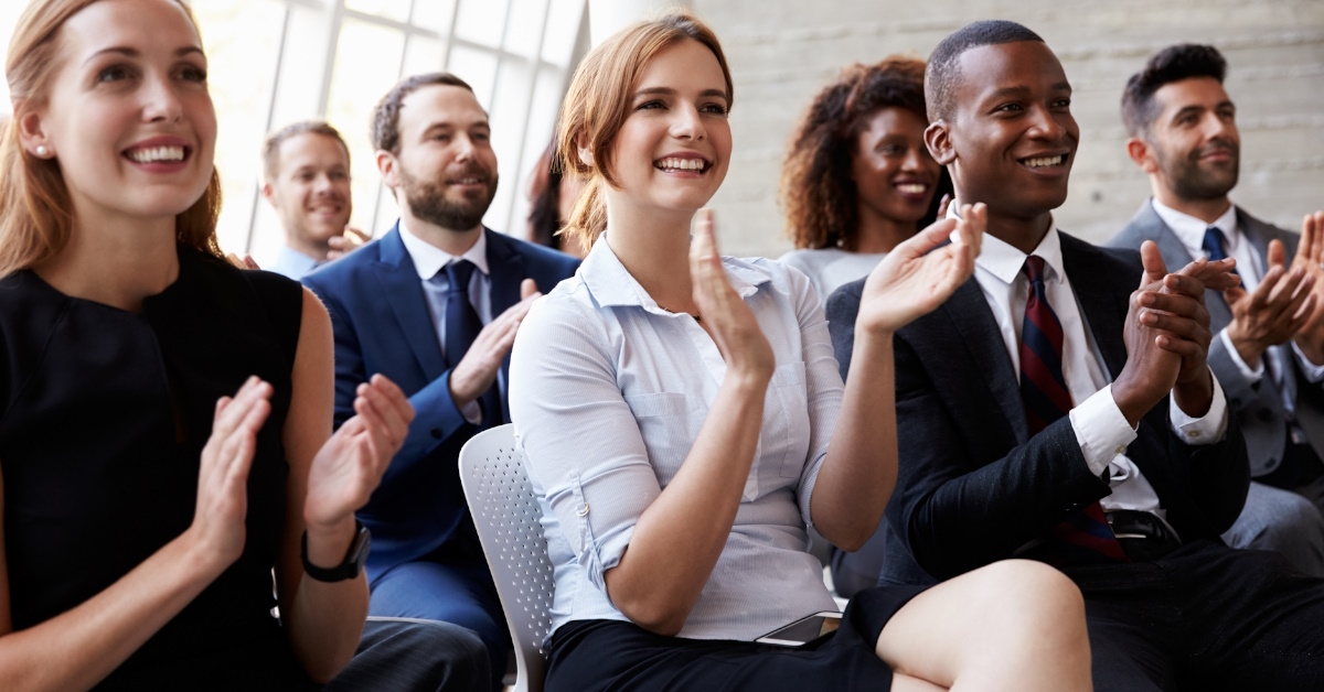 multi ethnic colleagues sitting at business conference applauding while smiling