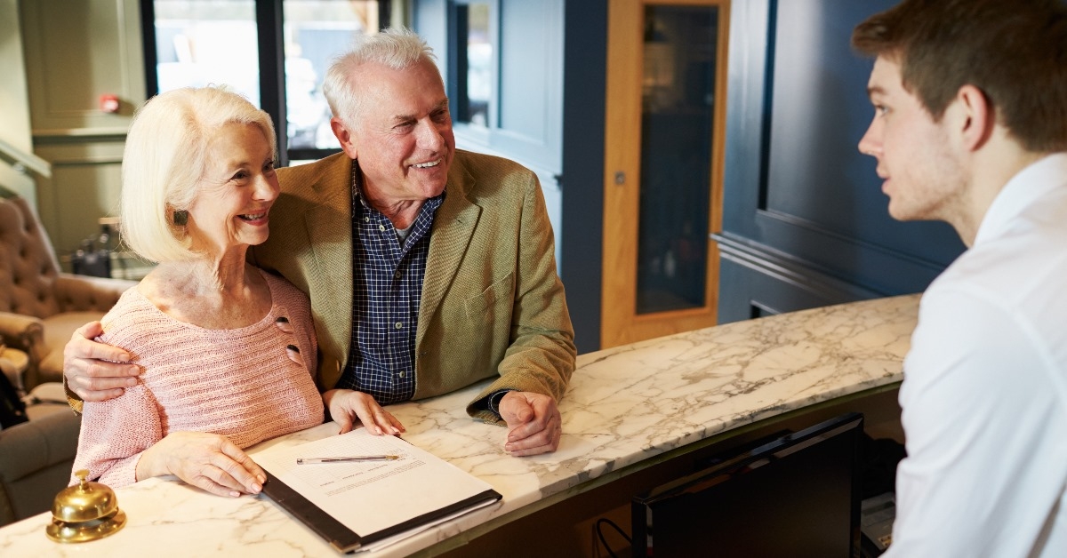 happy senior couple talking to male receptionist while checking in at hotel