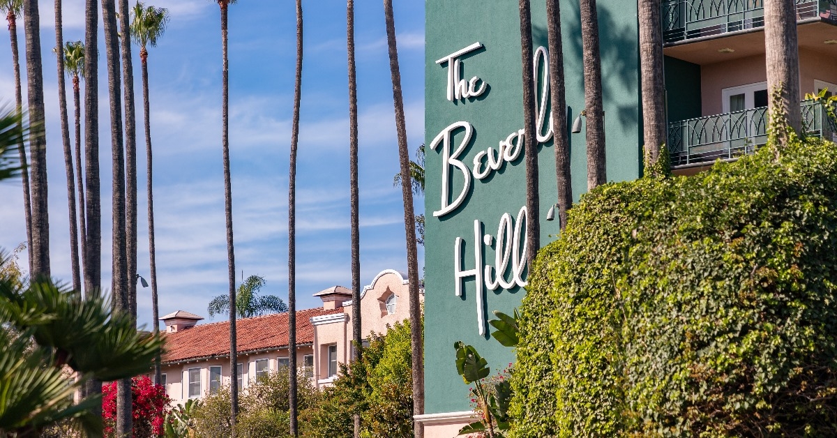 the beverly hills sign board on hotel surrounded with palm trees during day time