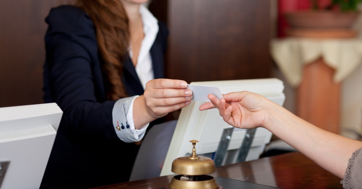 female guest receiving keys from female receptionist in hotel with bell on counter