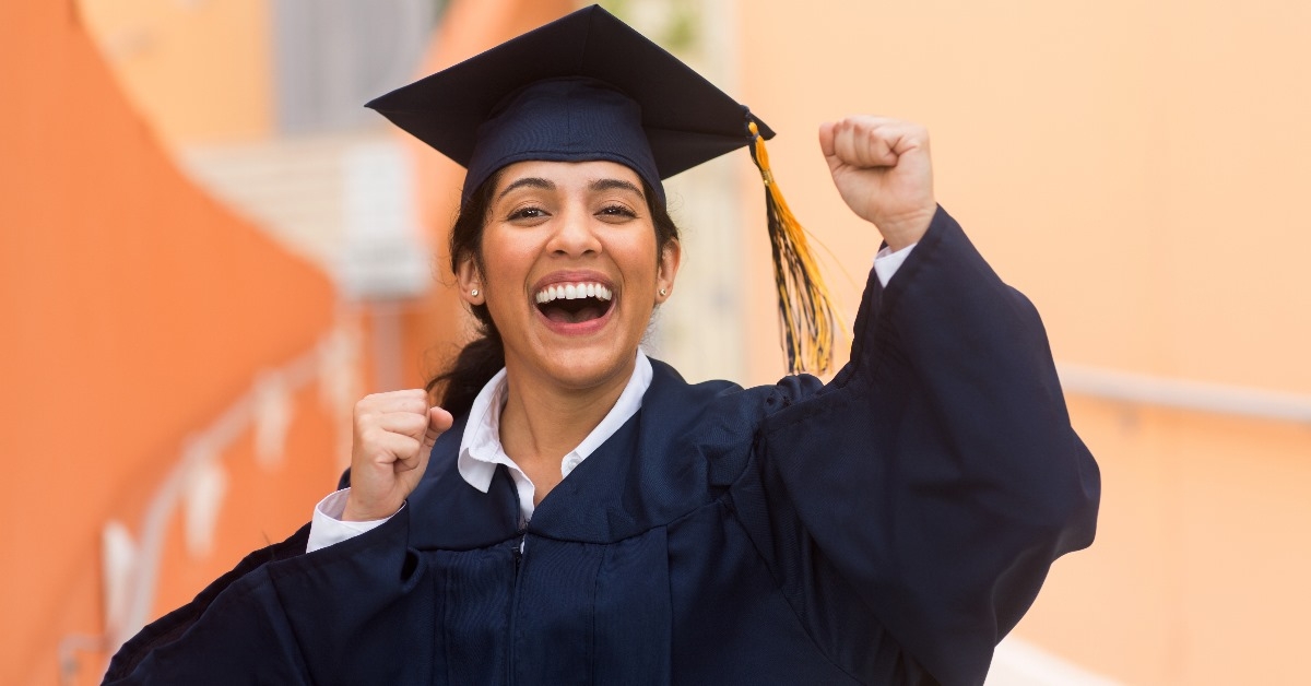 young woman cheering up while wearing graduation gown and hat